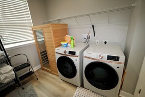 A laundry room with two Samsung washing machines, a drying rack, and a wooden cabinet.