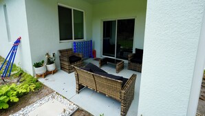 Un'area patio coperta con mobili in vimini, piante in vaso e una porta scorrevole in vetro.