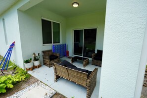 A covered patio area with wicker furniture, potted plants, and a sliding glass door. - Orlando Escape • Near Disney • 5 Bedrooms (Orlando)
