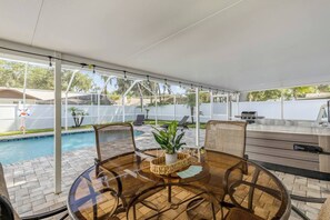 Ein überdachter Patio mit Pool, Gartenmöbeln und Grillplatz.