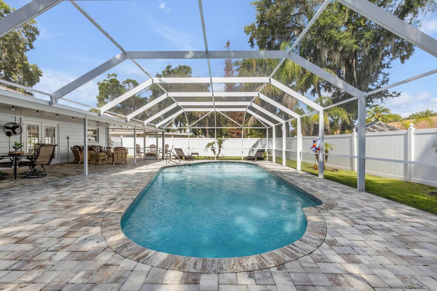 A covered outdoor swimming pool with a brick deck, surrounded by lounge chairs and a patio area.