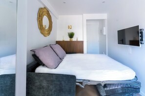 Ein zeitgemäßes Schlafzimmer mit Bett, Fernseher, Spiegel und Pflanze.