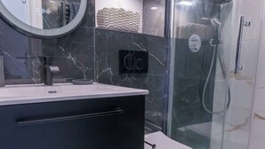 Un bagno moderno con un mobile lavabo nero, un water, una doccia vetrata e pareti in marmo.