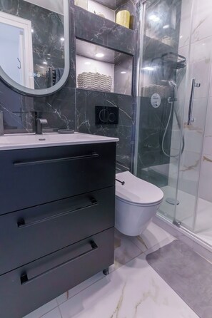Ein modernes Badezimmer mit einem schwarzen Waschtisch, einer Toilette, einer Duschkabine aus Glas und Marmorwänden.