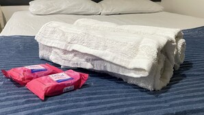 En säng med vita sängkläder, ett blårandigt överkast och två rosa förpackningar med säkerhetsbälten (LifeBelt) på sängen.