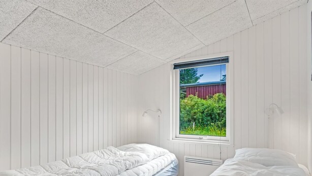 Quarto com duas camas, janela com vista para o verde e teto branco.