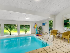 Ein Innenpool mit klaren Fenstern, einer farbenfrohen Skulptur, Korbstühlen und Blick auf Grünflächen.