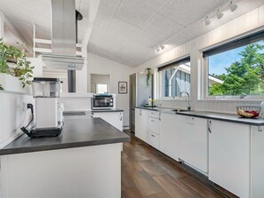 Una cocina moderna con armarios blancos, horno integrado y ventana con vistas a la vegetación.