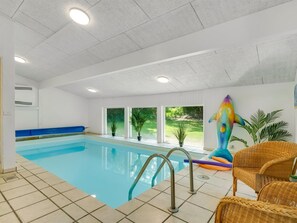 Una piscina interior con agua azul cristalina, un flotador de delfín colorido y sillas de mimbre.