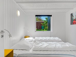 Un dormitorio con cama, ventana, lámpara y un cuadro en la pared.