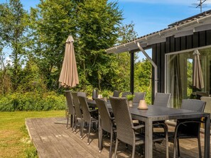 Ein Essbereich im Freien mit Tisch und Stühlen, umgeben von viel Grün und einem Gebäude mit großen Fenstern.