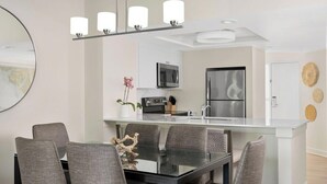 Una cocina moderna con una isla central, un comedor con mesa de vidrio y sillas tapizadas de gris, y un espejo grande sobre la isla.