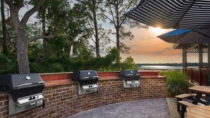 Un patio al aire libre con piso de ladrillo, tres parrillas para barbacoa y mesas de picnic.