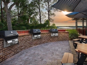 Eine Terrasse im Freien mit Backsteinpflasterung, drei Grillstationen und Picknicktischen.