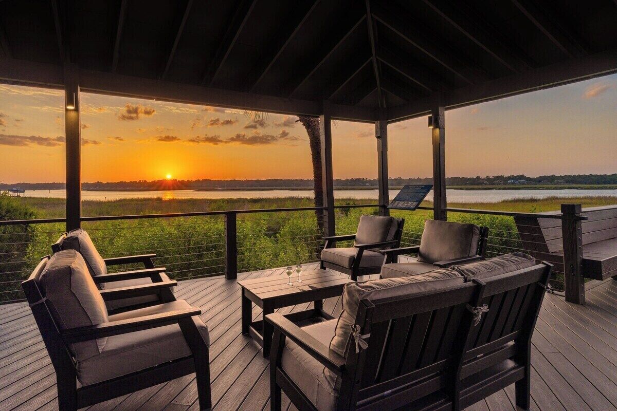 A covered outdoor seating area with a view of the sunset over a body of water.