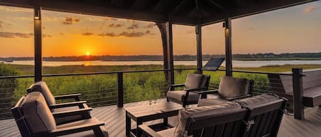A covered outdoor seating area with a view of the sunset over a body of water.
