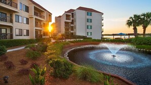 Un hotel con piscina, un patio iluminado por el sol y vistas al atardecer.
