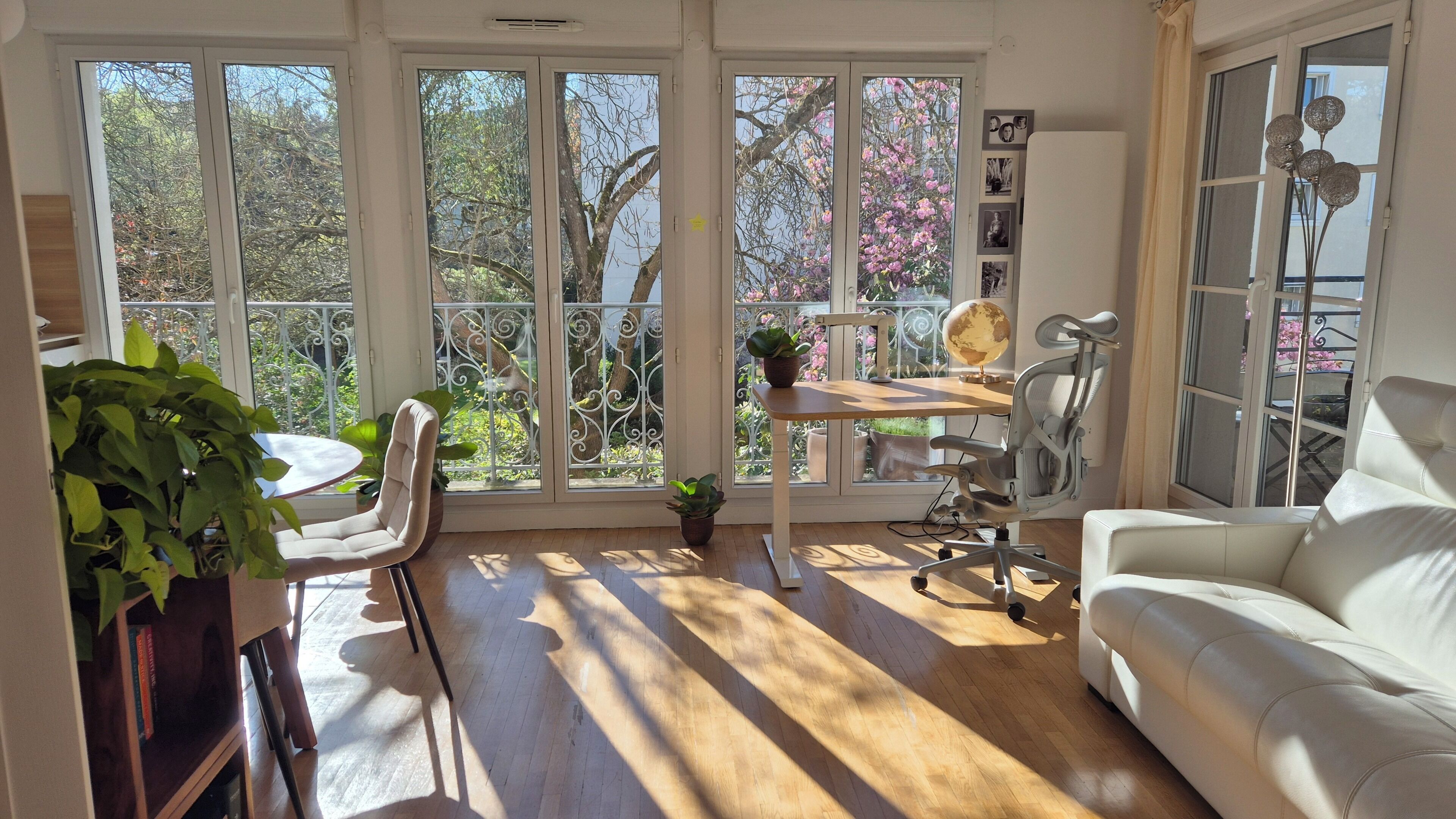 Een zonnige kamer met een witte bank, een eettafel met stoelen, een wereldbol en een potplant.