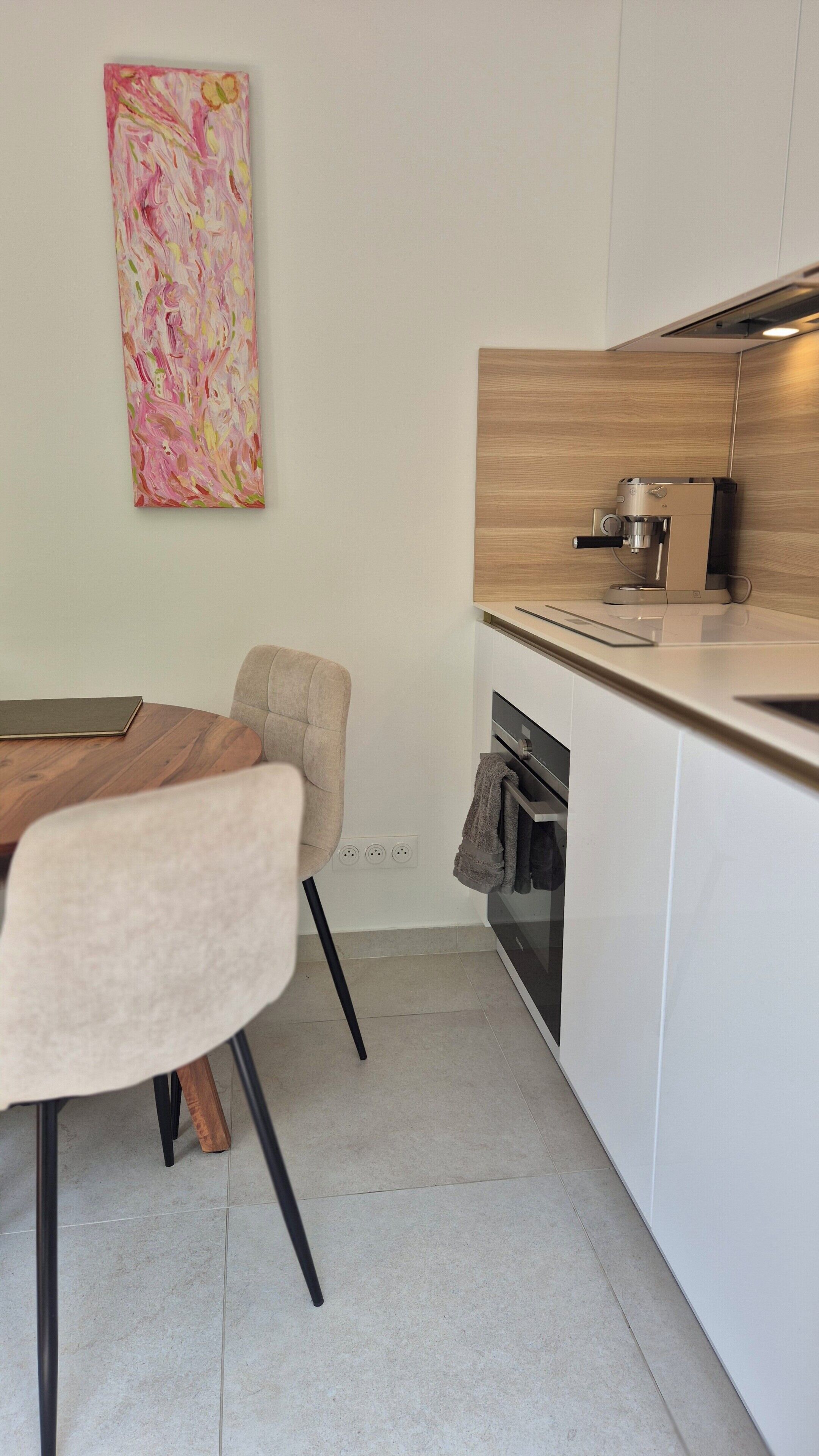 Een moderne keuken met een eethoek, een koffieapparaat en een groot abstract schilderij aan de muur.
