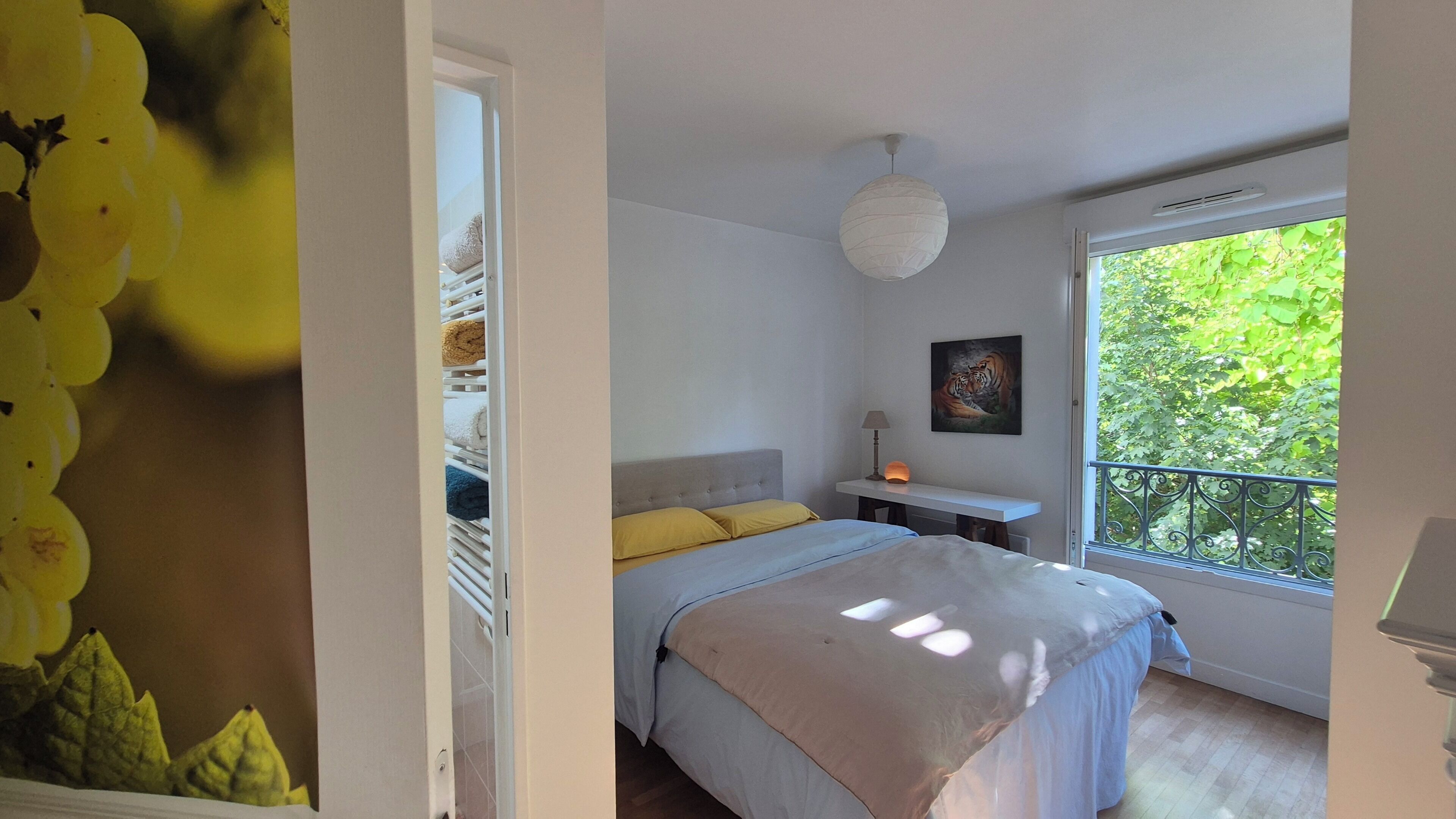 A bedroom with a bed, bedside table, lamp, and a window with a view of greenery.