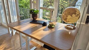 A wooden table with a laptop, a small speaker, a cup of coffee, a globe, and a potted plant. - 2-Room Apartment in Paris and Versailles with Balcony, Terrace, and Greenery (Le Plessis-Robinson)