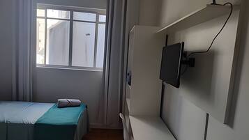 Quarto com cama, janela e televisão na parede.