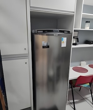 Ein Edelstahl-Kühlschrank in einer Küche mit einem weißen Schrank, einer Kaffeemaschine und einem roten Stuhl.