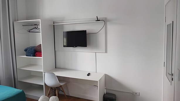 A bedroom with a bed, a desk, a chair, a TV mounted on the wall, and a wardrobe. - Quarto Triplo Augusta Paulista Frei Cane (São Paulo)