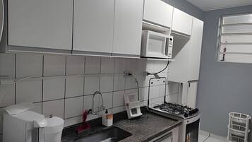 Uma cozinha com armários brancos, micro-ondas, fogão a gás, cafeteira e pia.