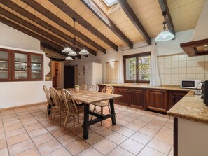 Une cuisine avec des meubles en bois, une table à manger avec des chaises, une fenêtre avec des rideaux et un plafond avec des poutres en bois.