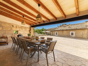 An outdoor dining area with stone walls, wooden beams, and a view of traditional buildings. - Can Toni by Interhome (Mancor de la Vall)