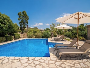 A swimming pool with lounge chairs and umbrellas, surrounded by greenery and stone flooring. - Can Toni by Interhome (Mancor de la Vall)