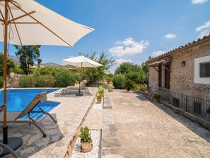 Un espace piscine agrémenté de chaises longues et de parasols, entouré de murs en pierre et de plantes en pot.