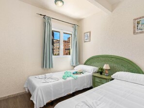 Una camera d'albergo con due letti, una finestra con tende, un comodino con una lampada e un quadro appeso al muro.