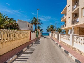 Eine schmale Straße mit Häusern an beiden Seiten, ein klarer Himmel und ein Blick auf das Meer in der Ferne.