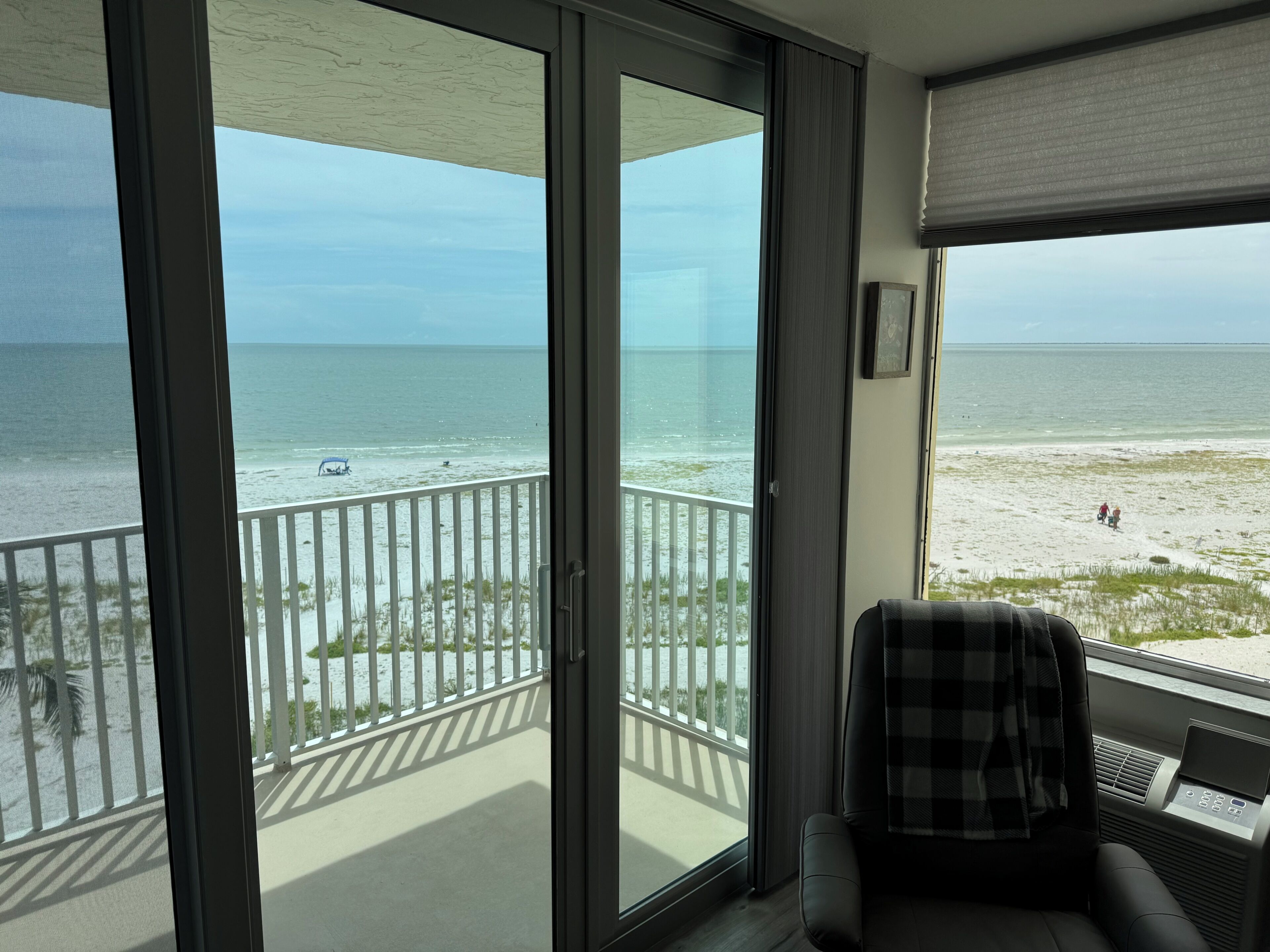 Een kamer met uitzicht op het strand, een schuifdeur, een stoel en een raam met uitzicht op de oceaan.