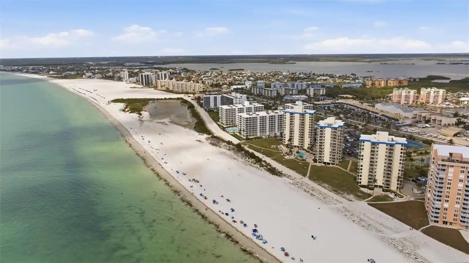 A coastal residential area with beachfront properties, clear water, and a mix of high-rise and low-rise buildings.