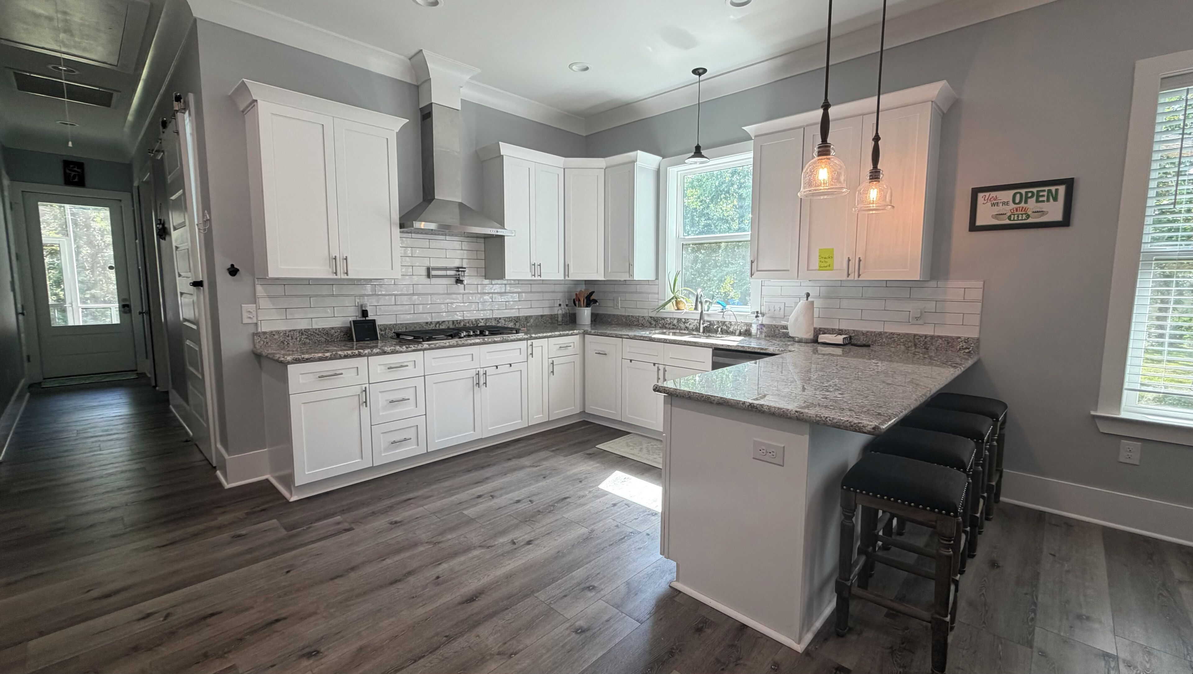 A modern kitchen with white cabinets, granite countertops, a central island, and pendant lighting.