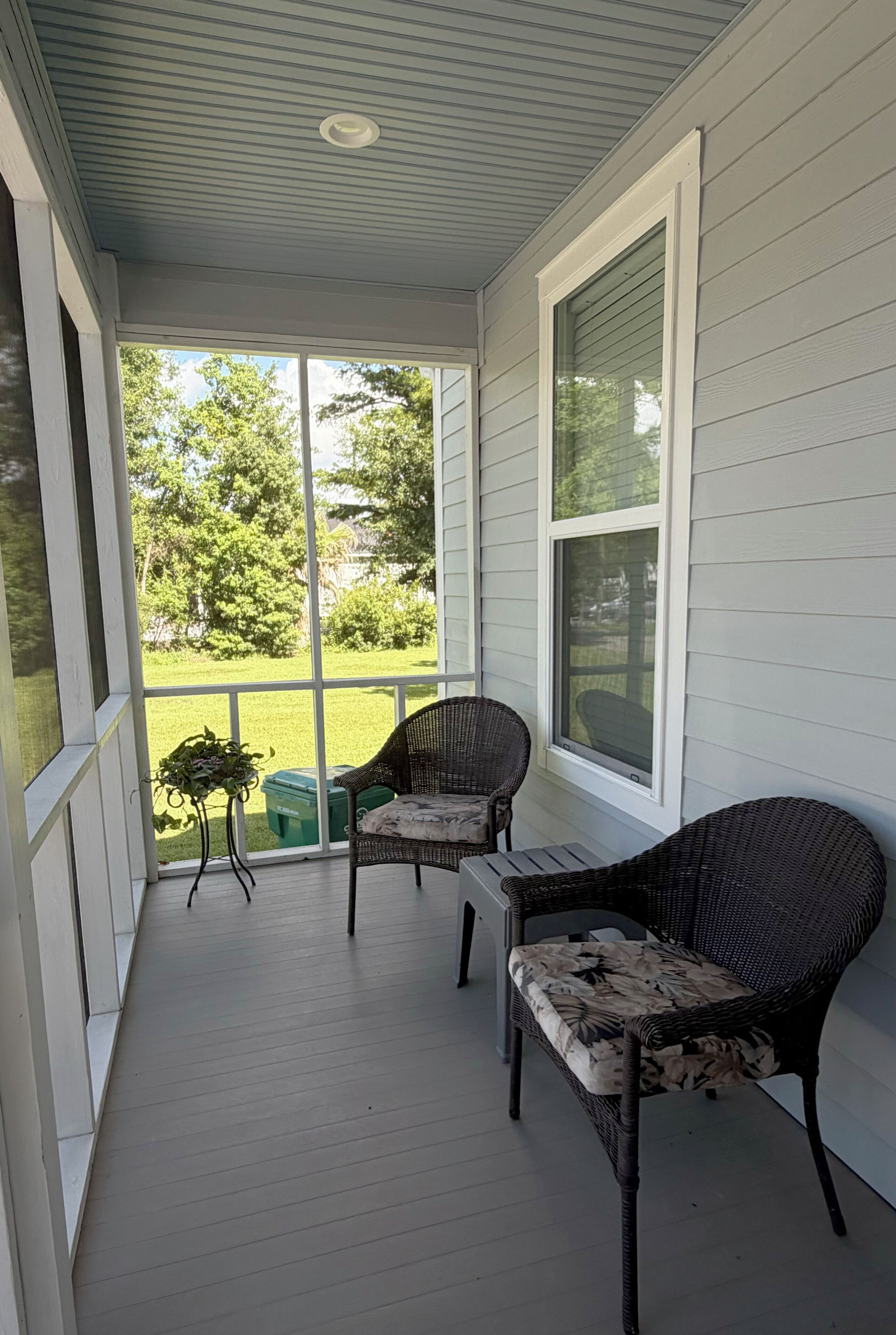 Eine überdachte Veranda mit zwei Korbstühlen, einem kleinen Tisch und einem Blumentopf.