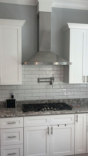 A kitchen with white cabinets, a stainless steel range hood, a granite countertop, and a gas stove. - Beautiful 2-bedroom, newly built home situated in historic Old Town Bay St Louis (Bay St. Louis)