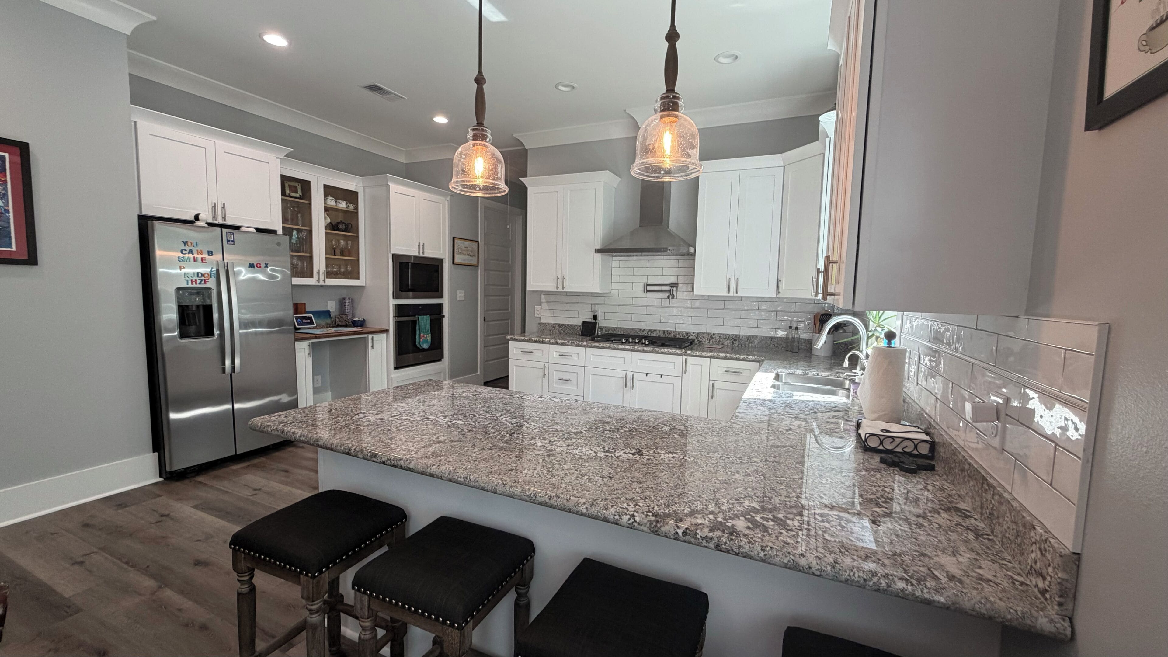 A modern kitchen with granite countertops, stainless steel appliances, and pendant lighting.