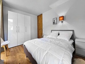 Ein Schlafzimmer mit Bett, Kleiderschrank, Nachttisch, einer Wandlampe und einer Holztür.