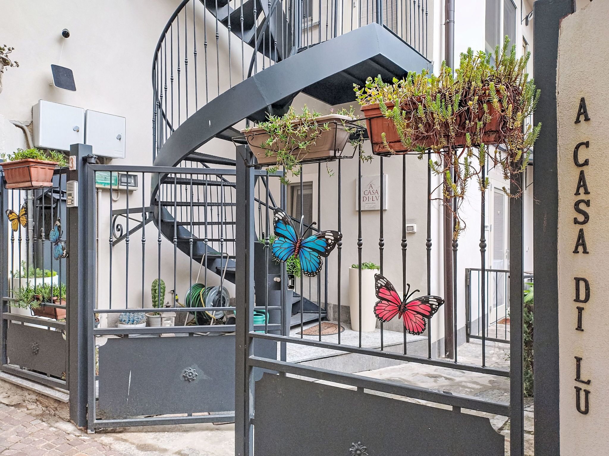 A gated entrance with a spiral staircase, potted plants, and butterfly decorations.