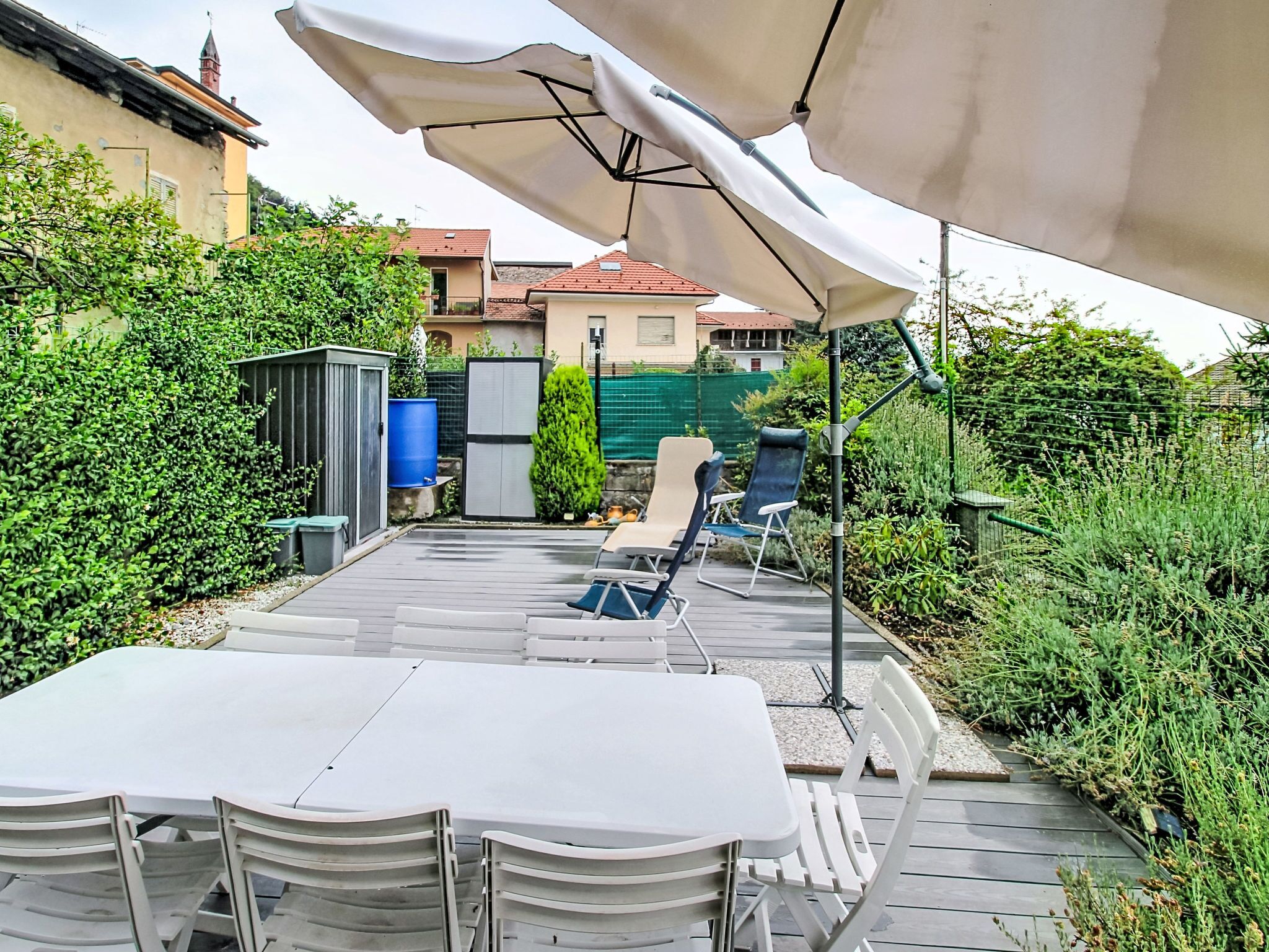 Un patio al aire libre con una mesa y sillas, rodeado de follaje y un edificio en el fondo.