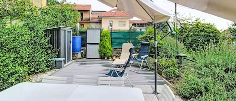 Un patio al aire libre con una mesa y sillas, rodeado de follaje y un edificio en el fondo.