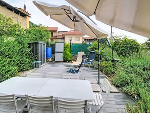 Eine Terrassengruppe mit Tisch und Stühlen, umgeben von Grünpflanzen und einem Gebäude im Hintergrund.