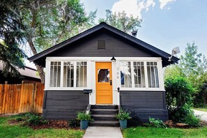 Una casa de dues plantes amb exterior fosc, detalls blancs i una porta principal groga.