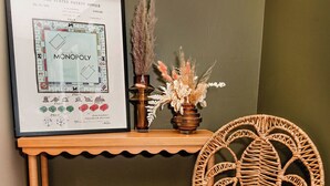 A framed Monopoly board game, a wicker chair, a plaid throw, and a small shelf with decorative items. - Little House on Taylor - 2 Bedroom Cottage in Walkable Downtown Location (Craig)