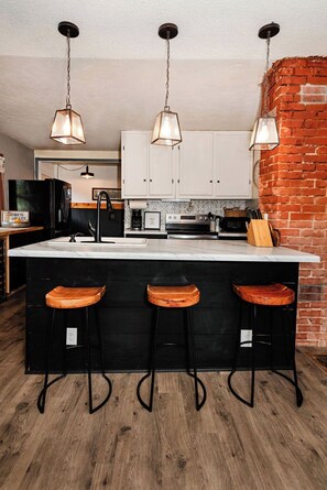 Une cuisine dotée d’un grand îlot central, de trois tabourets de bar et de luminaires suspendus.