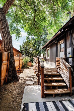 A wooden cabin with a porch, a large tree, and a gravel path.